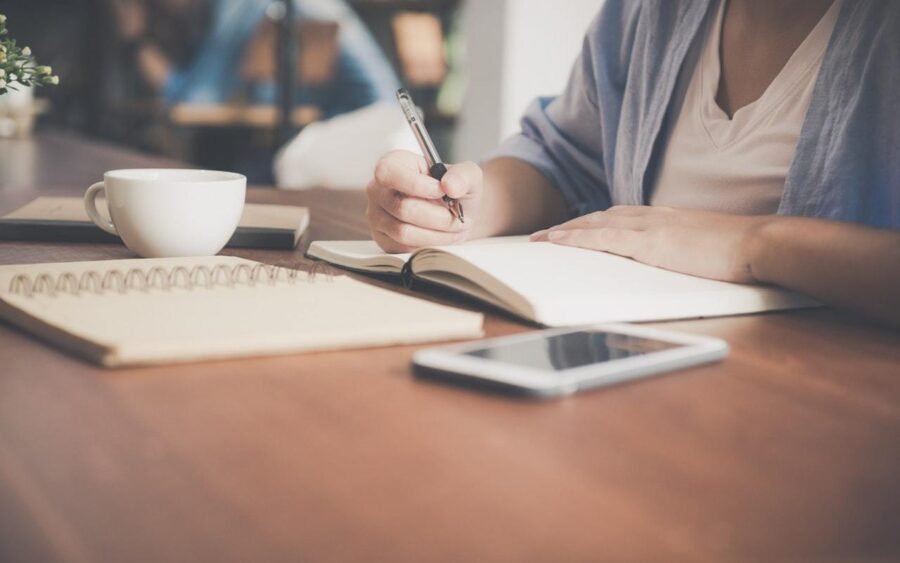 woman writing on a notebook beside teacup and tablet 733856